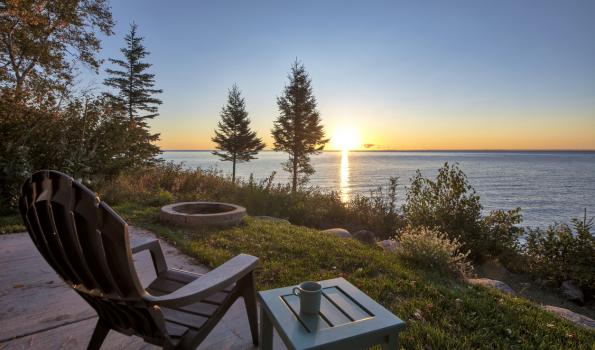 A picture of a chair and table overlooking trees and a lake during sunset