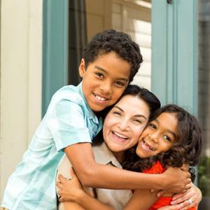 Mother and two school-aged children embrace warmly and smile