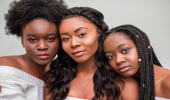 Three black women with their heads leaning against each other looking at the camera